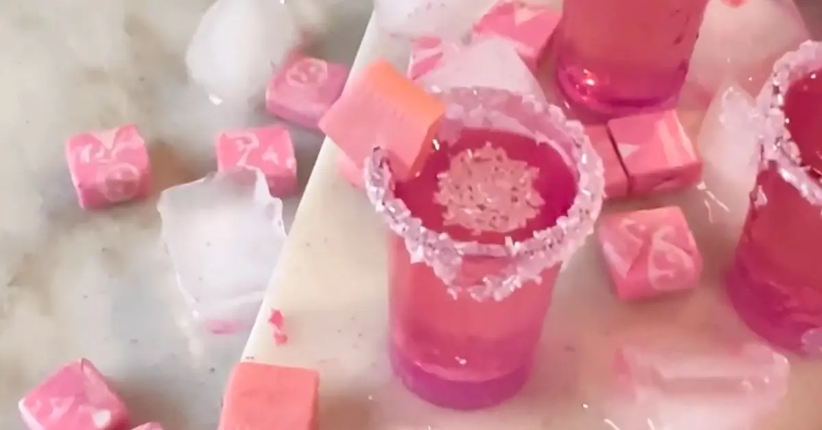 A refreshing pink drink in a shot glass with a candy on top